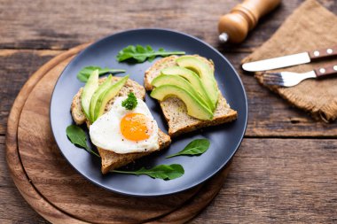Kızarmış yumurtalı Avokado Sandviçi Ahşap masada siyah tabakta