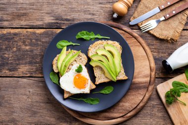 Kızarmış yumurtalı Avokado Sandviçi Ahşap masada siyah tabakta