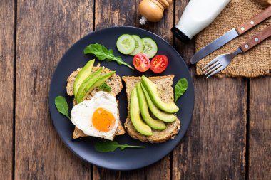 Kızarmış yumurtalı Avokado Sandviçi Ahşap masada siyah tabakta