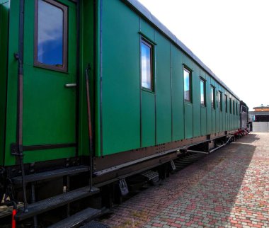 Geri dönüşümlü buharlı lokomotifin yeşil vagonu istasyon platformunda duruyor.