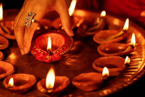 Happy Diwali background. Closeup image of female hand taking lit diya from a Puja thali. Concept for Indian traditional religious puja ritual, festive celebration, wedding.