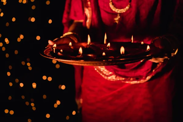 伝統的な赤いドレスとジュエリーを身に着けているインドの女性や花嫁 点灯Diyaや粘土ランプでいっぱいの法会を開催 ボケを背景に夜Diwaliを祝います — ストック写真