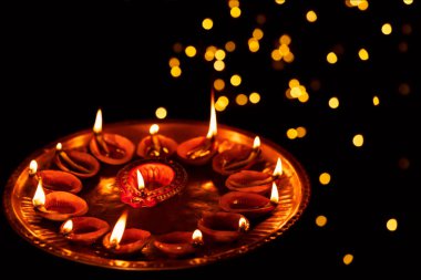 Lit clay diya oil lamps burning or illuminating on Diwali night in dark bokeh background at home. Concept for Indian Hindu festival celebration, ritualistic worship, ritual.