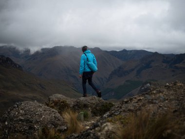 Tepelerin önündeki mavi ceketli yürüyüşçü tundra çayırları El Cajas Ulusal Parkı Cuenca Ekvador manzarası
