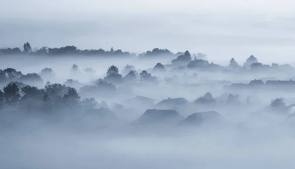 Village buildings houses and trees in low lying dense fog clouds moody morning haze in Gemeinlebarn Lower Austria — Stock Photo, Image