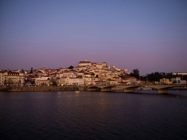 Tepedeki eski Coimbra tarihi merkezinin panoramik günbatımı manzarası ve Ponte de Santa Clara köprüsü nehir Mondego Portekiz