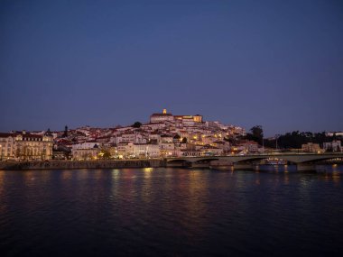 Tepedeki eski Coimbra tarihi merkezinin panoramik günbatımı manzarası ve Ponte de Santa Clara köprüsü nehir Mondego Portekiz