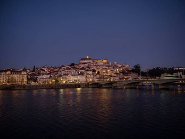 Tepedeki eski Coimbra tarihi merkezinin panoramik günbatımı manzarası ve Ponte de Santa Clara köprüsü nehir Mondego Portekiz