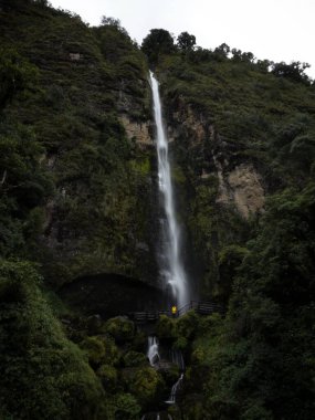 Güney Amerika 'da Cuenca Azuay Ekvador yakınlarındaki El Chorro de Giron şelalesinin önündeki sarı ceketli genç adam.