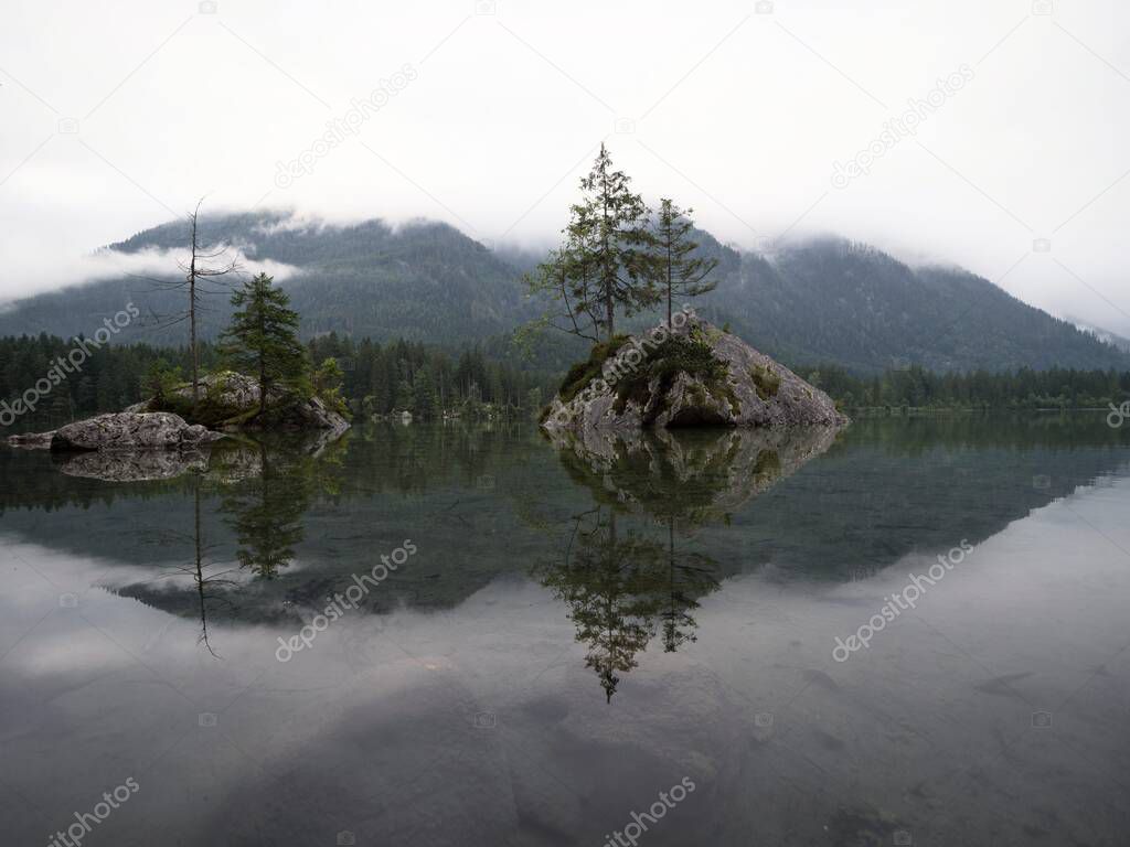 Tree island reflection in alpine mountain lake Hintersee cloudy mood Ramsau Berchtesgadener Land Bavaria Germany
