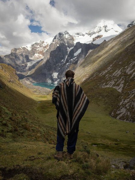 Young male hiker in traditional poncho at Cordillera Huayhuash Circuit andes mountain Gangrajanca lake Ancash Peru