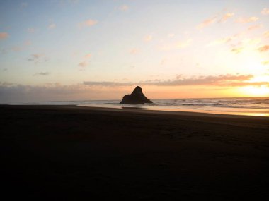Panorama sunset view of Paratahi Island rock on black sand Karekare Beach West Auckland North Island New Zealand clipart