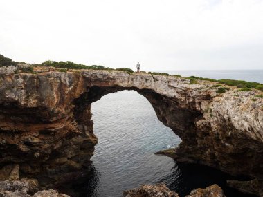 Erkek turist yürüyüşçüsü Cala Varques Calo Blanc Mallorca Akdeniz 'de doğal bir kaya köprüsünde
