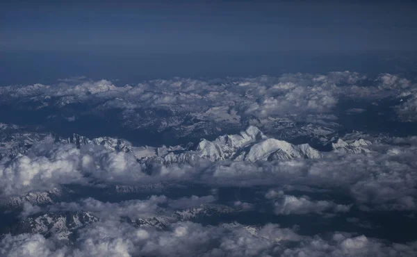 Alpine snow capped mountain peaks summit nature panorama landscape with clouds from airplane over Alps Europe