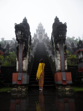 Genç bayan turist, Endonezya Asya Bali 'deki Pura Penataran Agung Lempuyang Hindu tapınağının merdivenlerinin önünde duruyor.
