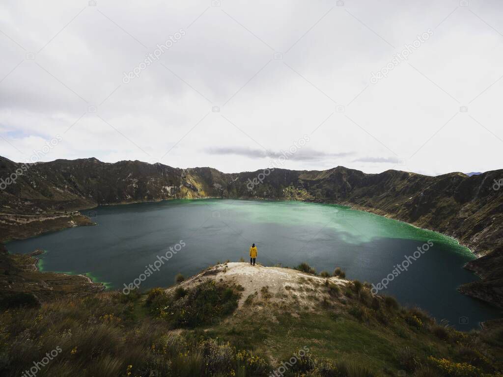 Young male hiker in yellow jacket at andean volcano caldera crater lake Quilotoa rim ridge loop in Pujili Cotopaxi Ecuador andes South America