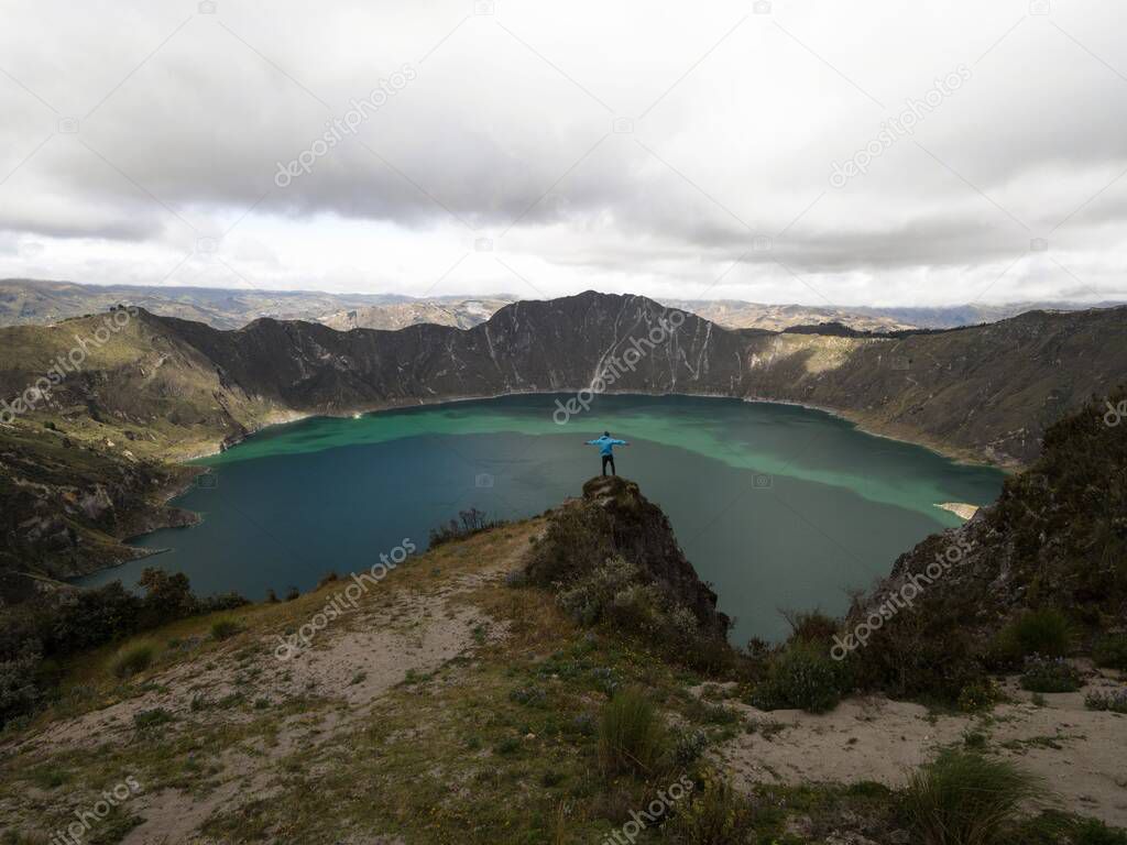 Young male hiker in blue jacket at andean volcano caldera crater lake Quilotoa rim ridge loop in Pujili Cotopaxi Ecuador andes South America