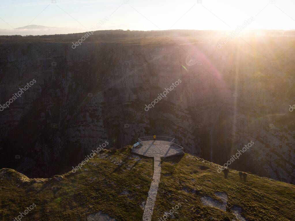 Aerial panorama view of tourist person in yellow jacket on viewing platform observation deck on cliff edge at Salto del Nervion river waterfall Delika Canyon Alava Araba, Basque Country Spain Europe