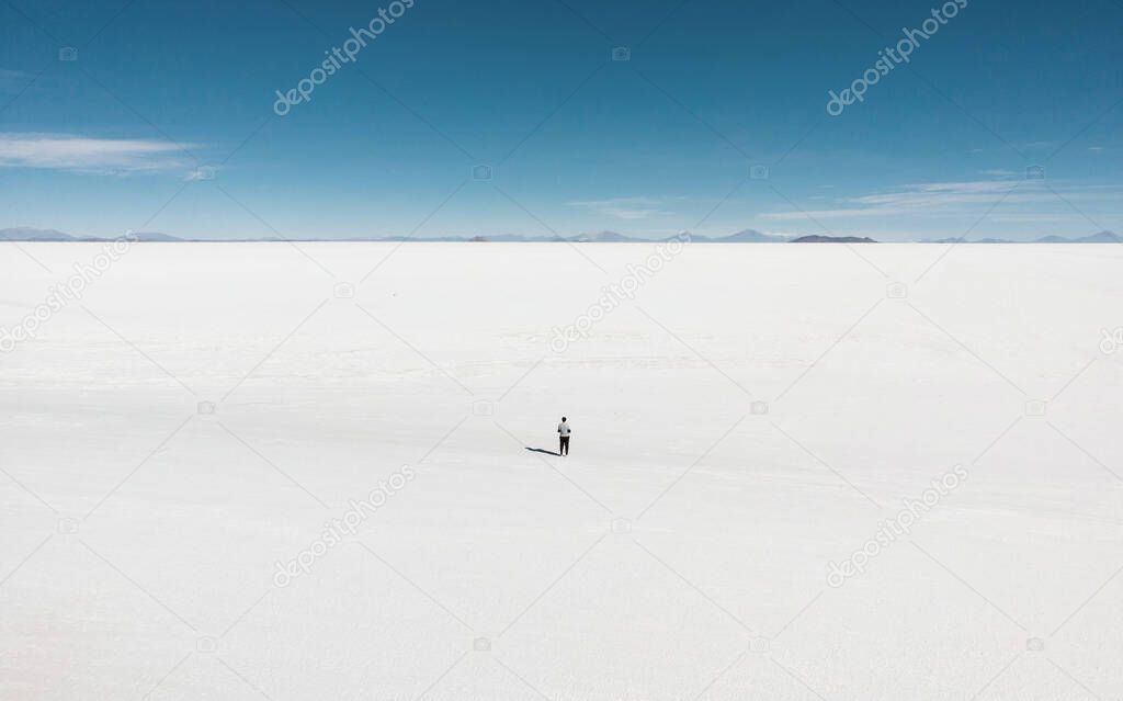 One isolated male tourist enjoying endless boundless infinite vastness width expanse of white salt flat lake Salar de Uyuni in Potosi Bolivia South America
