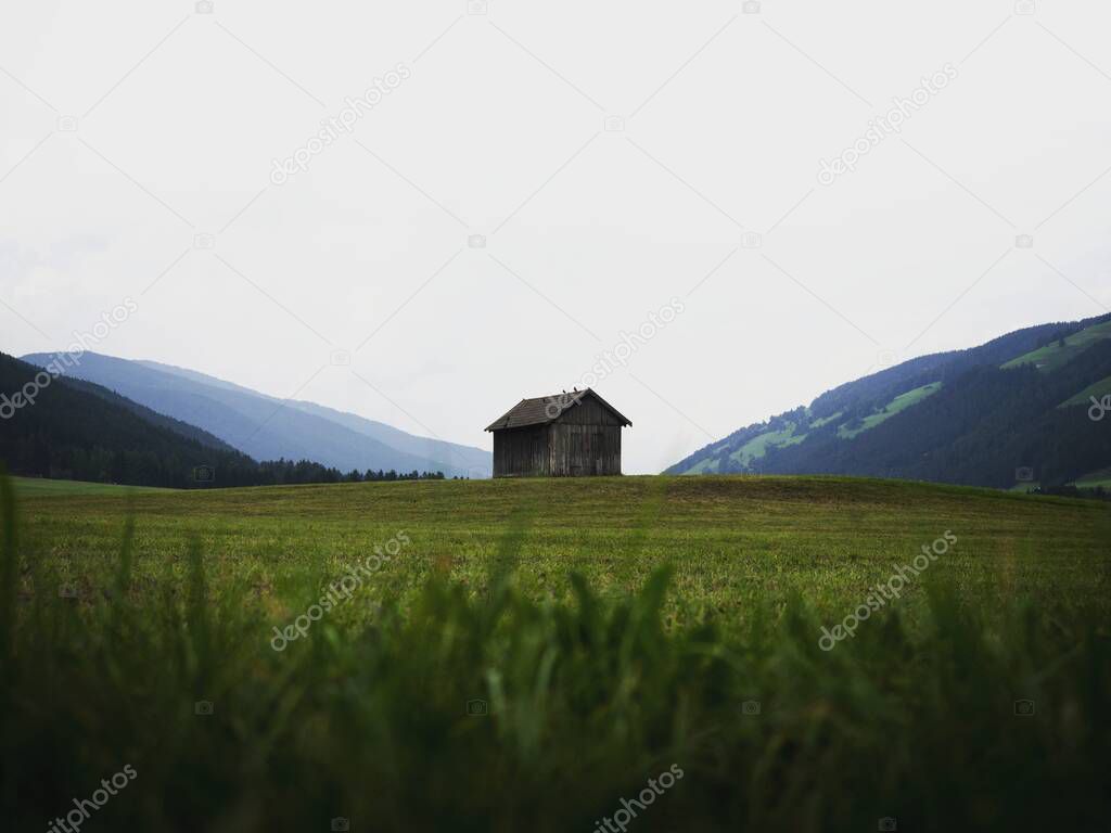 Alpine mountain panorama of idyllic remote wooden shed cabin in green grass field meadow of Dolomites alps South Tyrol Italy Europe