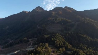 Sonbaharda dağlardaki güzel ormanın üzerinde hava manzaralı bir uçuş. Gün batımında dağların renkli manzarası. Dağlarda gezin ve eğlenin