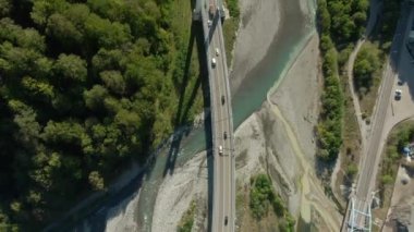 Ormanlarla çevrili fırtınalı bir nehrin üstündeki dağ geçidinde yüksek hızlı bir otoyolun üzerinde uçuyorlar. Arabanızla seyahat edin. Dağ nehri üzerindeki modern köprünün güzel manzarası..