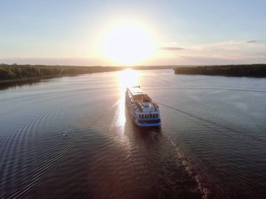 Hava manzaralı yolcu gemisi gün batımında güneşle buluşmak için yelken açar. Geminin güzel manzarası. Suyun üzerindeki güneşin yansıması.
