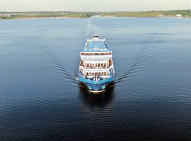 Hava manzaralı yolcu gemisi, yazın gün batımında güzel yeşil bir ormanla çevrili nehir boyunca yelken açar. Seyahat Gemisi Tatili