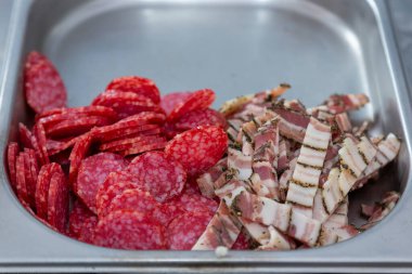 Pizza için et malzemeleri - salam ve domuz pastırması metal bir kasede kesilmiş. Dilimlenmiş salam ve pastırma. Soğuk yenmiş İtalyan eti jambonu, pastırma..