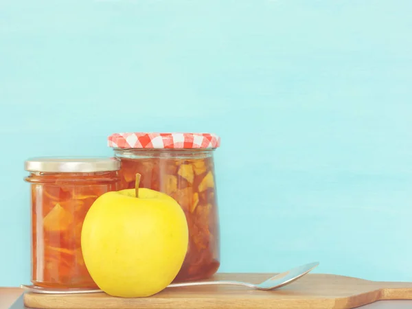 Two closed jars of jam, yellow apple and spoon — Stock Photo, Image