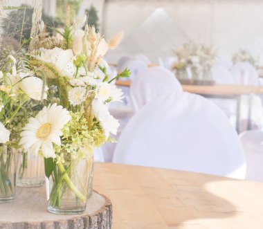 Cam bir vazoda hafif gerbera ve beyaz sandalyeli küçük yeşil bir buket.