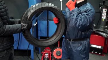 Bir adam yeni bir lastiği tamir için bir lastik düzenleyicisinin eline veriyor. Lastik tamircisinin yeni lastiği var, lastik tamircisi tamir için lastiği alıyor. Orta bölüm çekimi