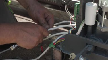 Elektrik kablolarını otomatik sürgülü kapı motorunun kontrol paneline bağlayan profesyonel bir teknisyenin yakın çekimi.