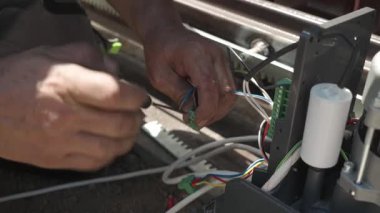 Elektrik kablolarını otomatik sürgülü kapı motorunun kontrol paneline bağlayan profesyonel bir teknisyenin yakın çekimi.