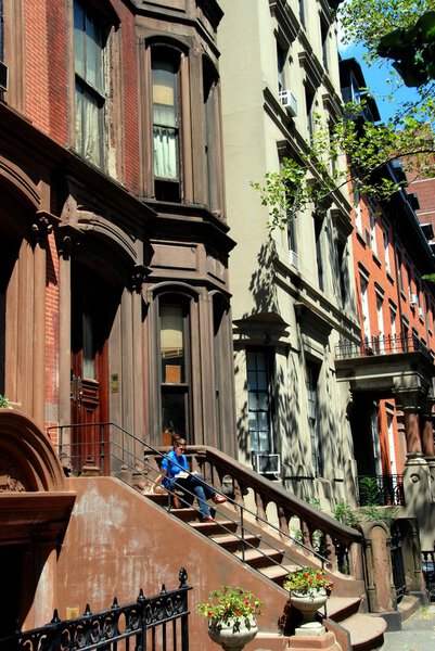 BROOKLYN HEIGHTS, NY: Woman reading on the stoop of a classic 19th century brownstone on Henry Street