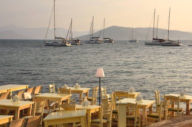 Yunanistan 'ın Aegina şehrinde gün batımında sahilde akşam yemeği için masalar hazırlanıyor.
