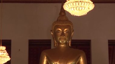 Bangkok 'ta. Tayland. Budist tapınağı, büyük Buda heykeli, yüzüne yakın çekim. Kamera yavaşça uzaklaşır ve heykelin altında oturan rahipleri gösterir.. 