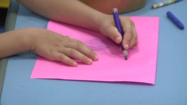 Bir çocuk renkli kalemle bir çiçek çizer.