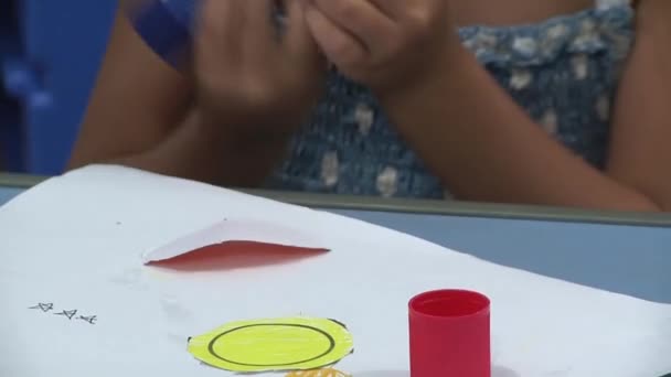 幼稚園では少女が紙から切り取られた楕円形を鉛筆で描いたものです 二人の少年がプロセスを見ている — ストック動画