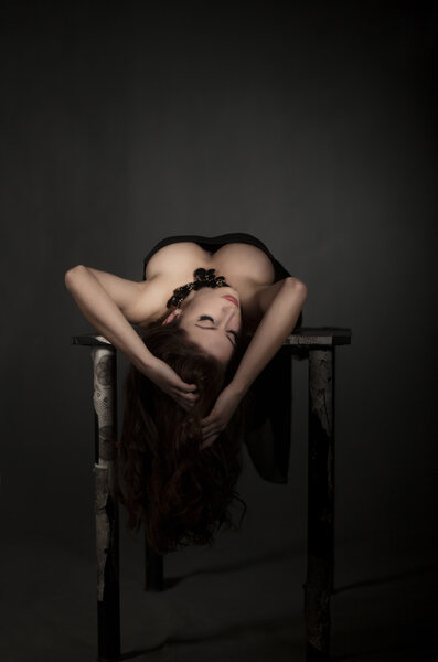 Beautiful brunette girl lying on a vintage table on dark background