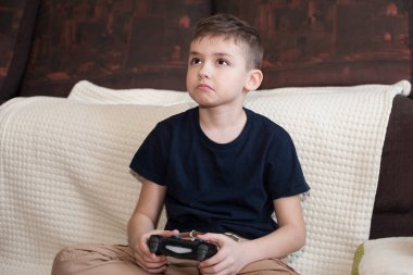 Avrupalı görünümlü bir çocuk üzgün bir suratla oyun konsolu oynuyor