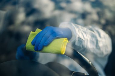 Dezenfekte uzmanı sarı halılı bir arabanın direksiyonunu temizliyor. Sağlık görevlisi, aracın sürücü koltuğunu dezenfekte eder. Covid-19 yayılmayı önlüyor. Sağlık kavramı