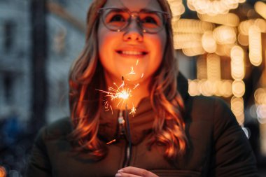 Genç ve çekici bir kadın elinde maytaplarla dışarıda duruyor ve yeni yılı ve Noel 'i kutluyor. Kış bayramı festivali havası. Kadın mutlu olur. Aşk ve mutluluk kavramı