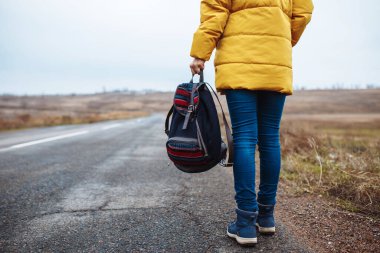 Sırt çantasında bir sırt çantasıyla yalnız başına yolda yürüyen bir kadının yakın plan görüntüsü. Genç kadın kış ya da sonbahar sezonunda seyahat eder. Otostop, gezi, seyahat konsepti