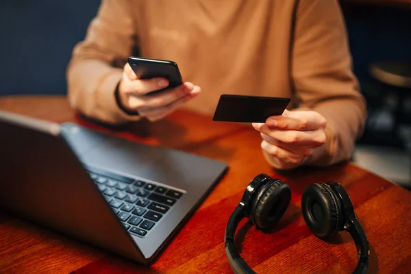 Shopping and online payment using laptop and credit card. Man sitting in a cafe wearing casual clothes buys goods and pays via internet with a black debit card. New normal and technologies concept