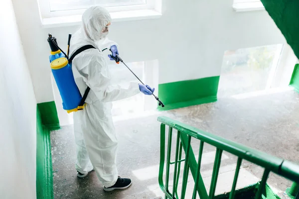 Tehlikeli madde giysisi giyen profesyonel hijyenik işçiler bir apartman girişini dezenfekte ediyor. Yerleşim bölgelerinde koronavirüs önleme önlemleri. Yeni normal ve Covid-19 yayılma konseptini durdur