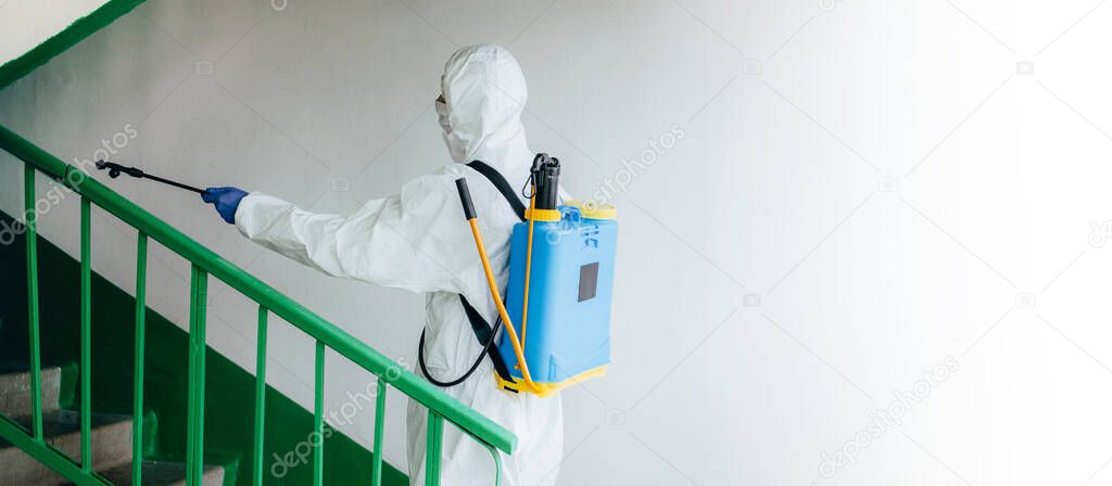 Wide shot. Sanitary professional worker in protective suit disinfects a staircase entryway block of flats. Coronavirus prevention measures at residential areas. New normal and stop Covid-19 spread