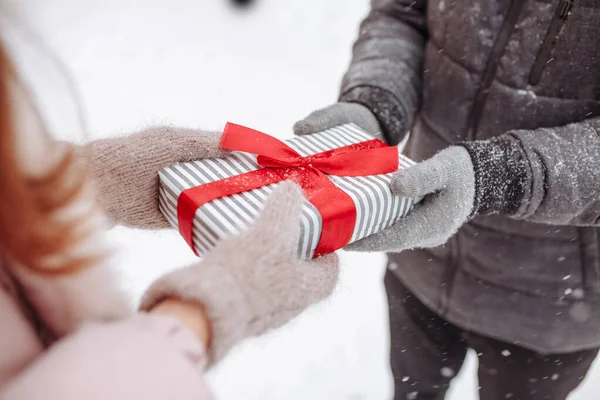 在雪地的冬季公园里 这对可爱的夫妇穿着羊毛衫 送给对方一份礼物 一个男人和一个女人手里拿着红弓的条纹盒 情人节的概念 女人的日子 — 图库照片