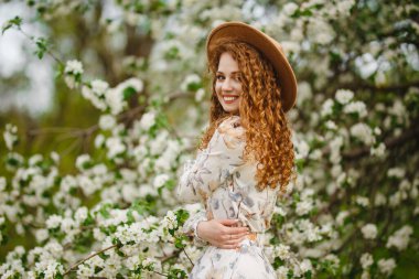 Genç bir kadının çiçek açan elma ağaçlarının arasında mutlu olması. Bir kız baharın tadını çıkarır ve ağaçlardaki beyaz çiçekleri koklar. Mevsim değişimi ve taze gün konsepti