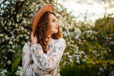 Genç kız çiçek açan bahçede güneşli bir bahar gününün tadını çıkarıyor. Elma ağaçlarının beyaz çiçekleri arasında yürüyor. Bej şapkalı ve beyaz elbiseli bir kadın gün batımında parkta özgürlüğü hissediyor.